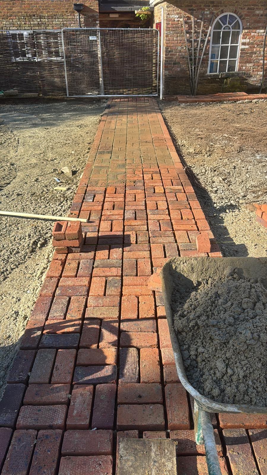 Workers laying a basket weave brick path on a construction site